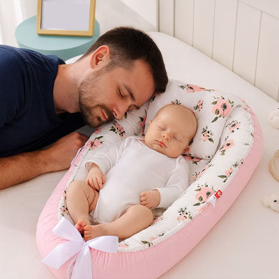 bébé dort dans réducteur de lit à cote de son pére